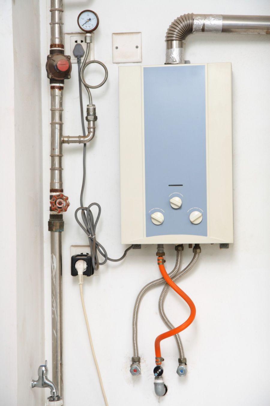 Wall-mounted tankless water heater with connected pipes, valves, and venting in a utility room